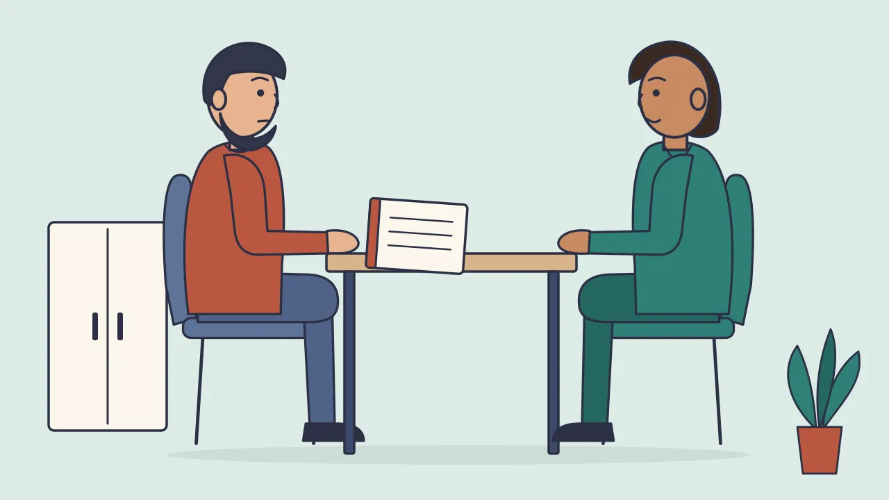 A clinician and an adult patient talk across a desk in a calm clinic room, with a cabinet and a small plant behind them