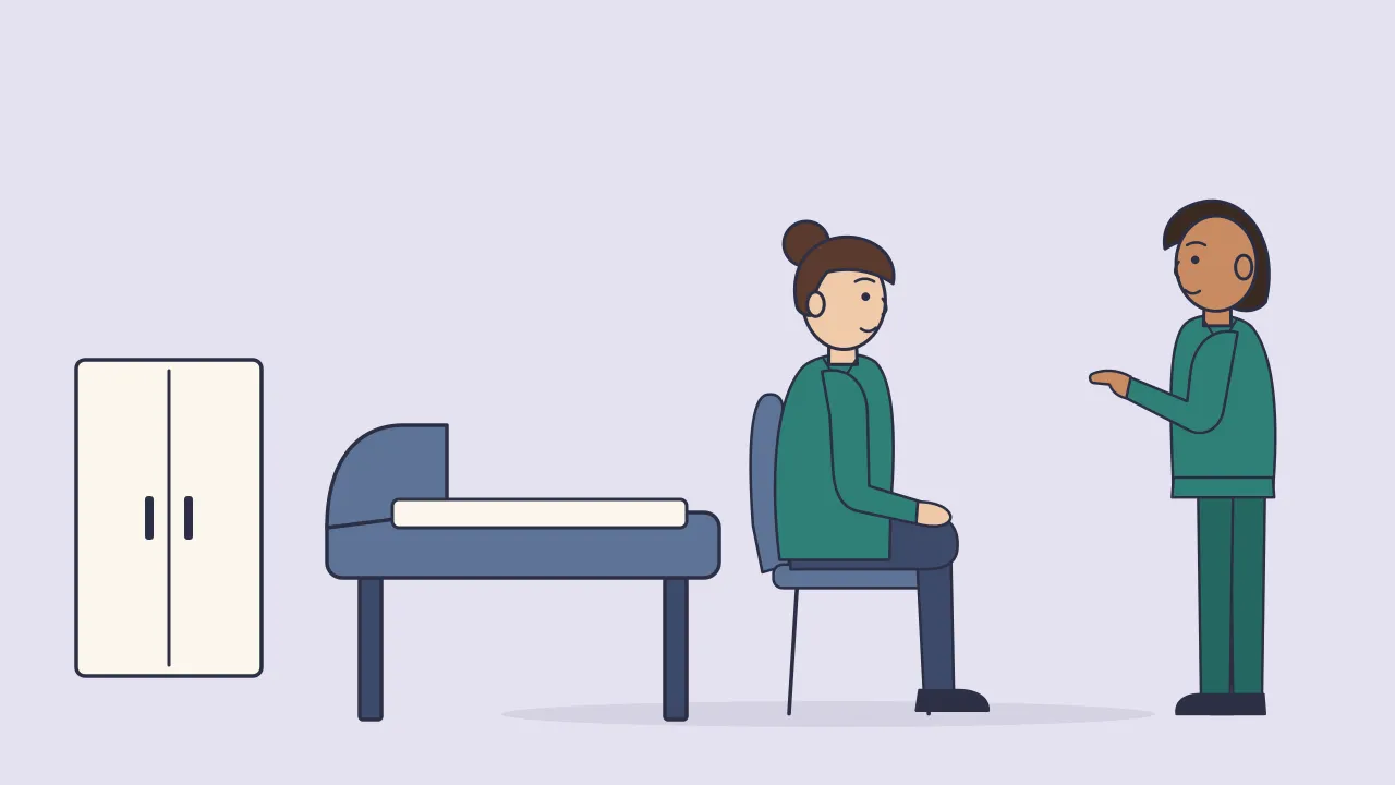 A doctor in a clinic room talks with a seated adult patient, with an examination couch and a cabinet behind them