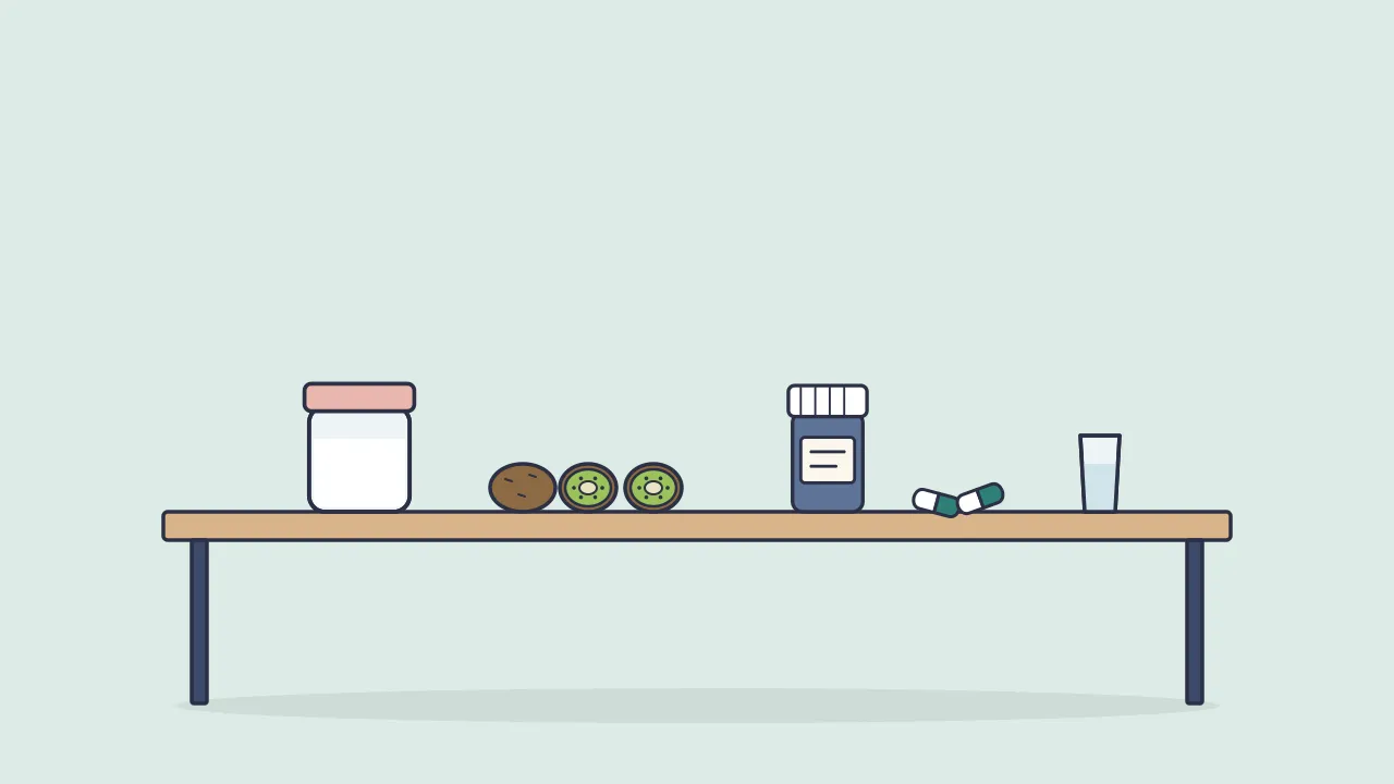 A kitchen table with a jar of yogurt, whole and halved kiwifruit, a supplement bottle with a few capsules and a glass of water