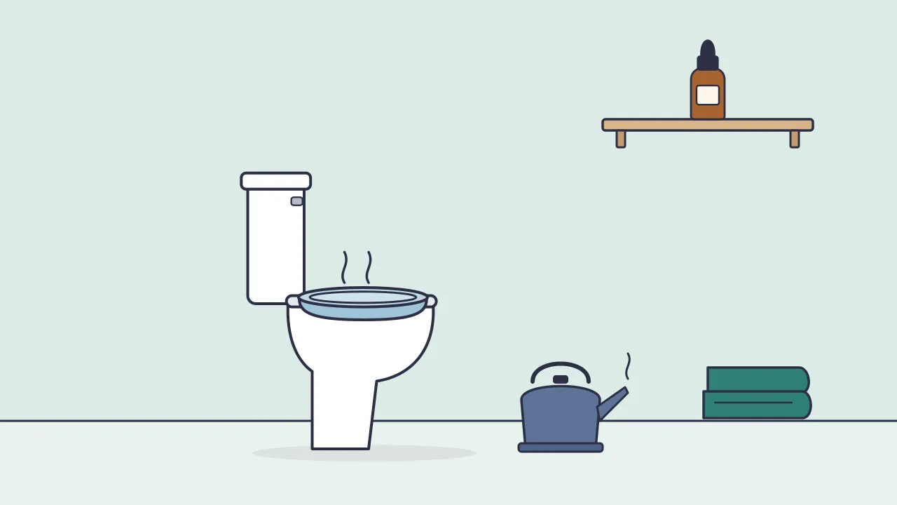 A sitz bath basin on a toilet seat beside a kettle and a folded towel, with a small dropper bottle left on a high shelf