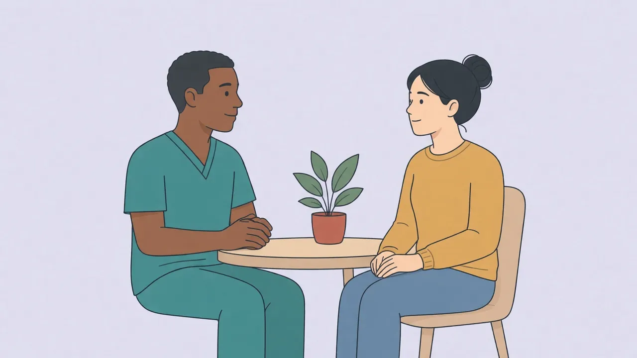 A clinician in a teal top and an adult patient in a mustard sweater sit in an exam room, both fully clothed, talking across a small desk