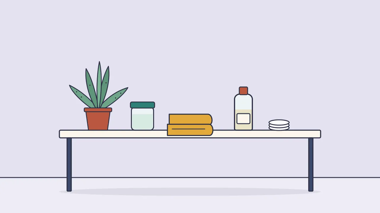 A bathroom counter with a potted aloe plant and a small jar of gel on the left and a bottle of witch hazel with cotton pads on the right, separated by a folded towel
